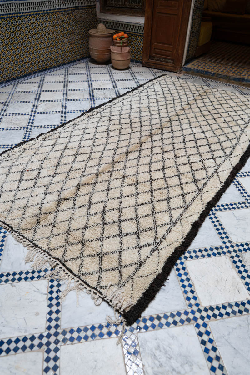Pereinteinen marokkolainen riad, jossa  graafinen vintage-matto ja taustalla puiset ovet