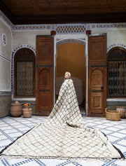 Woman standing in a decorative room with patterned moroccan rug and wooden doors.