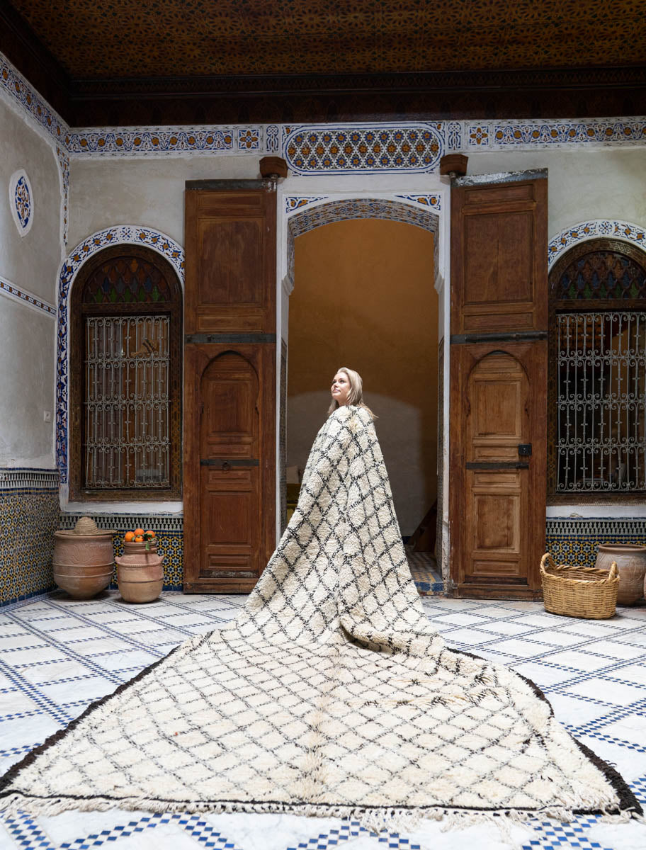Woman standing in a decorative room with patterned moroccan rug and wooden doors.