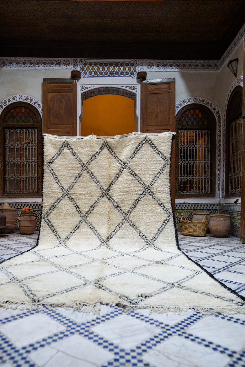 Beige and black diamond patterned rug on a tiled floor with decorative arches in the background.