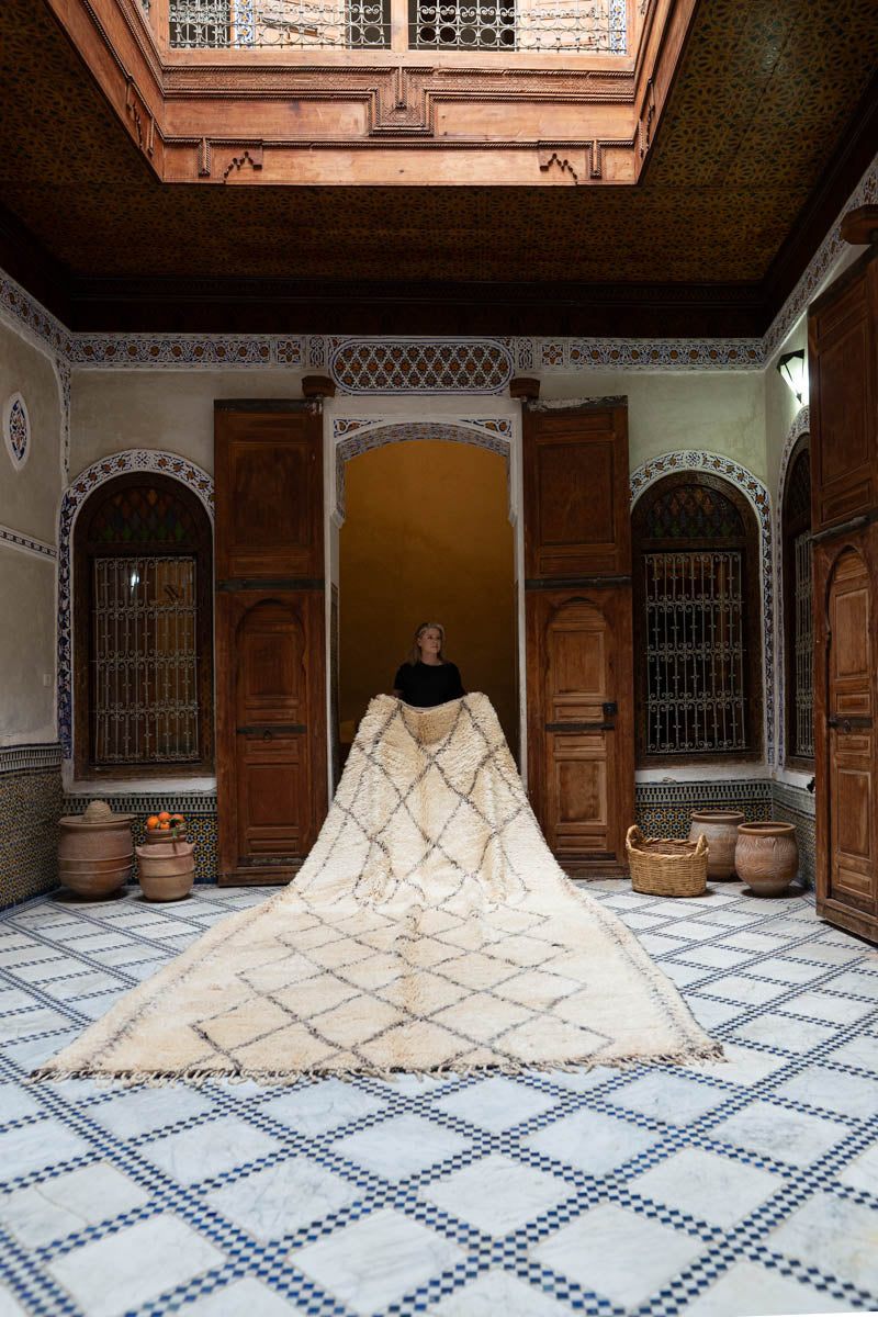 Large white Moroccan rug with geometric pattern on a checkered floor in a room with wooden doors and decorative elements.