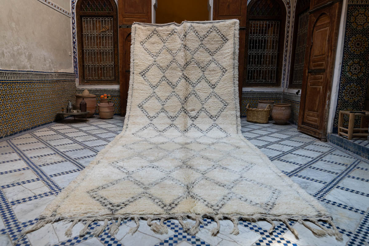 Beige and brown patterned Moroccan rug on a blue and white checkered floor with wooden doors and decorative elements in the background.