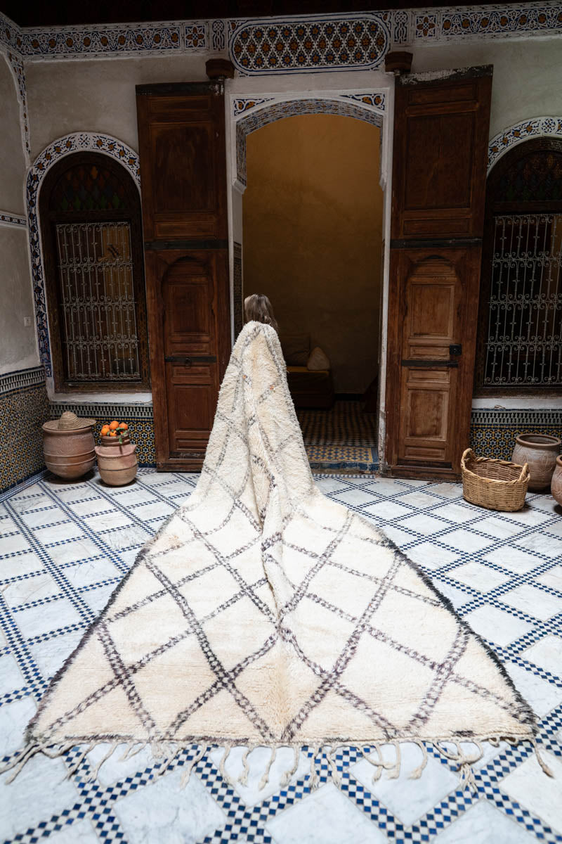 Person standing in a room with a large geometric-patterned rug on a checkered floor.