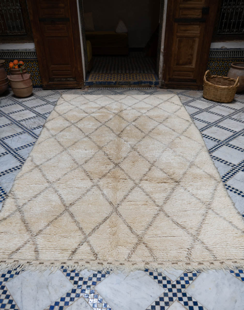 Beige diamond patterned Moroccan vintage Beni Ouarain rug on a checkered floor with wooden doors in the background