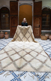Woman standing behind a large woven Moroccan Beni Ouarain rug in a room with wooden doors and decorative elements.