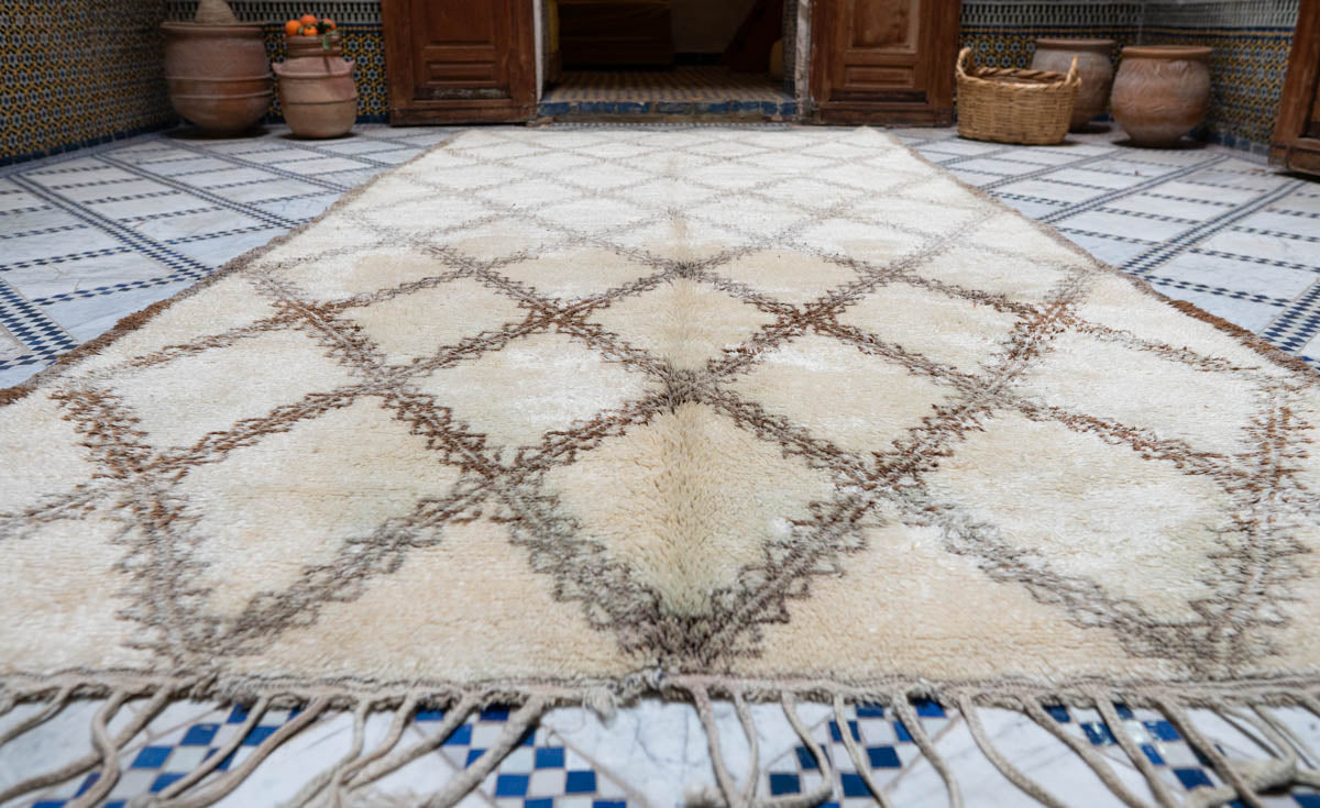 Beige and brown diamond patterned Moroccan Beni Ouarain Vintage rug on a tiled floor with decorative pots in the background.
