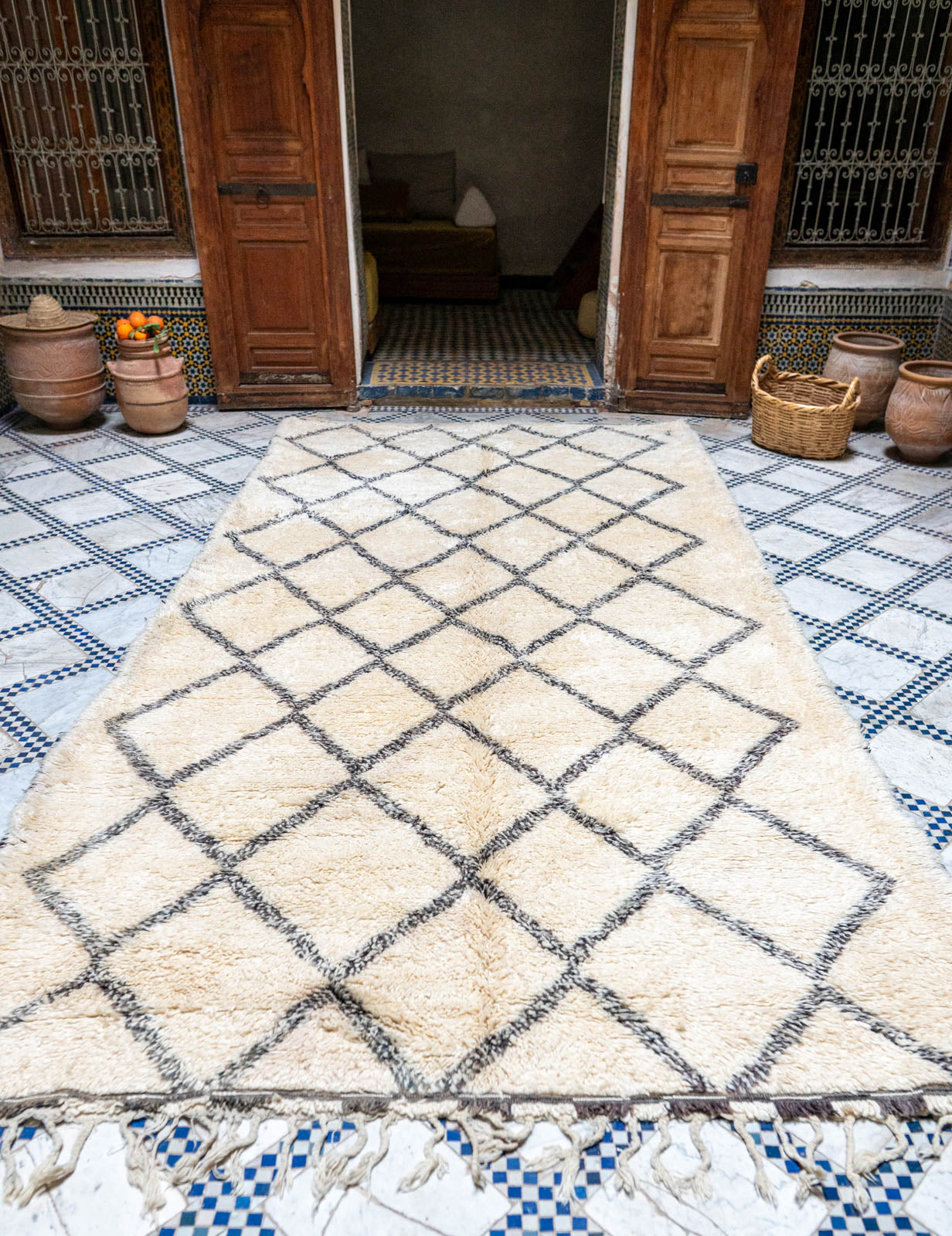 Natural white diamond patterned rug on a blue and white checkered floor with wooden doors in the background.