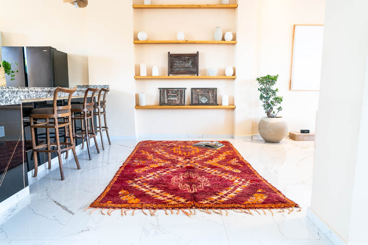Red patterned rug on a white floor in a modern kitchen with wooden shelves and decor.