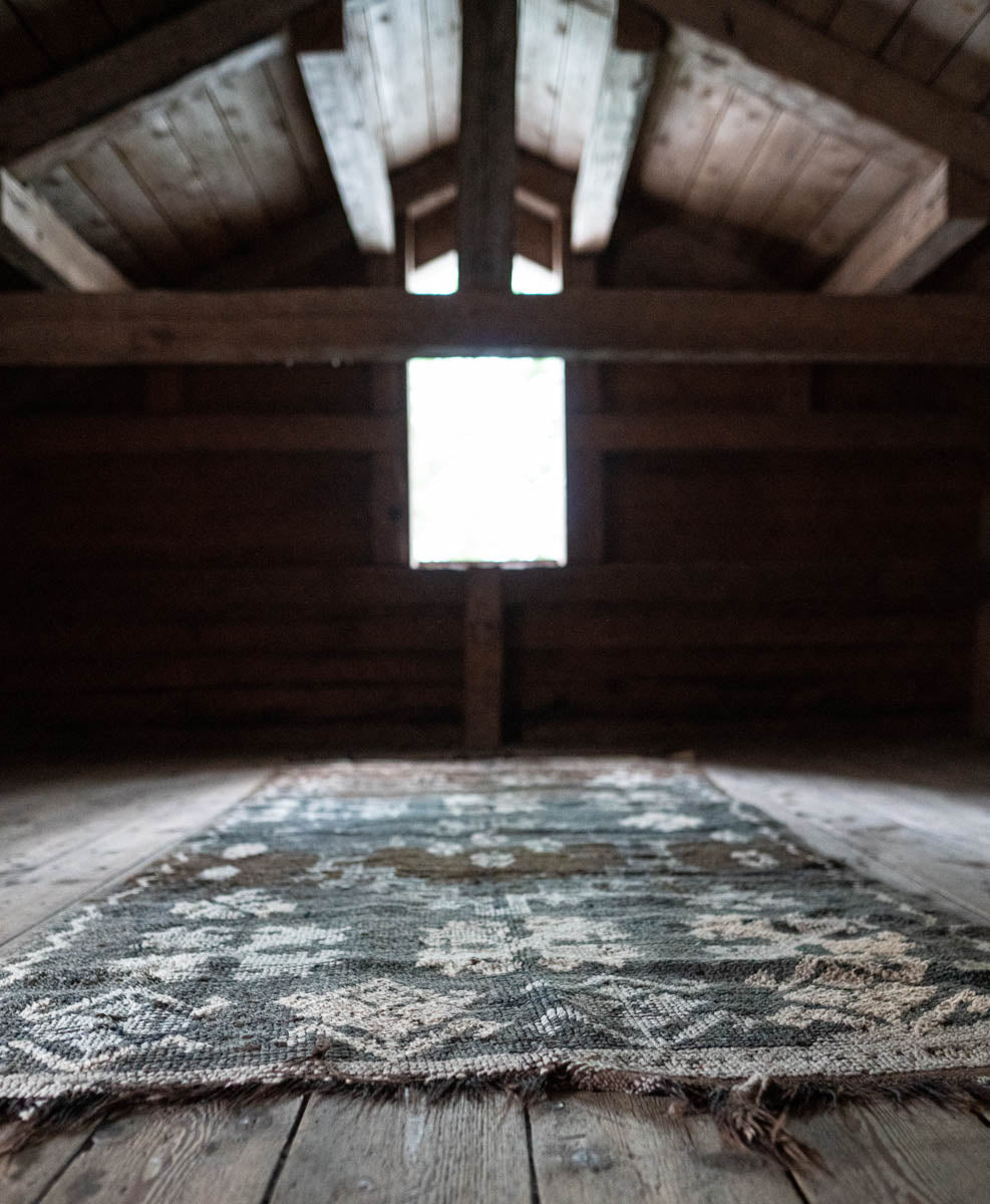 Woven rug on wooden floor with wooden beams and light source in the background
