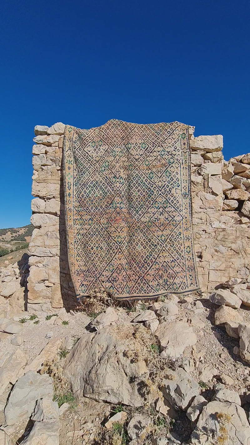 Handwoven Moroccan rug hanging against an old stone wall, moving softly in the mountain breeze.
